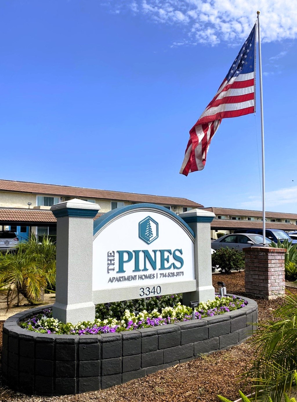 a flag flies above the pines apartments sign in front of a building