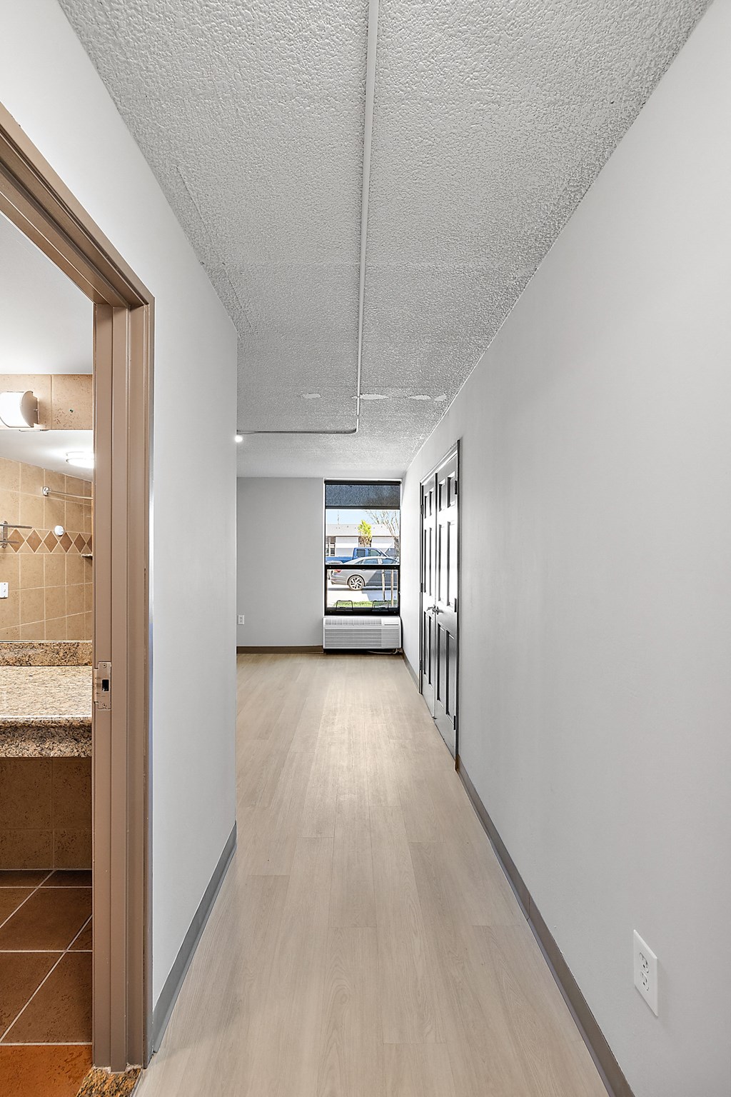 a long hallway with white walls and wood flooring and a wooden door
