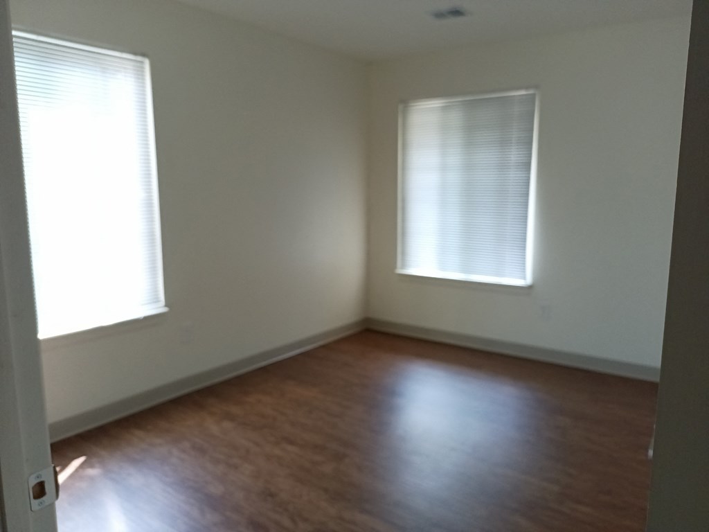 an empty room with wood floors and two windows