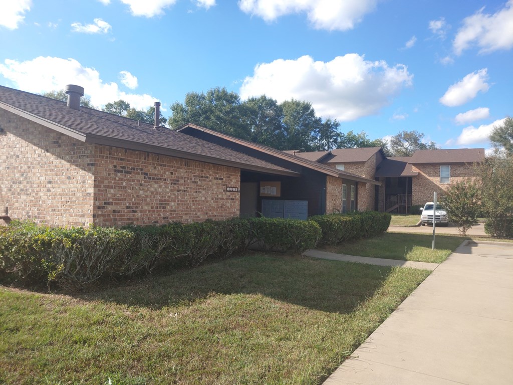 the front of a brick house with a lawn and a sidewalk