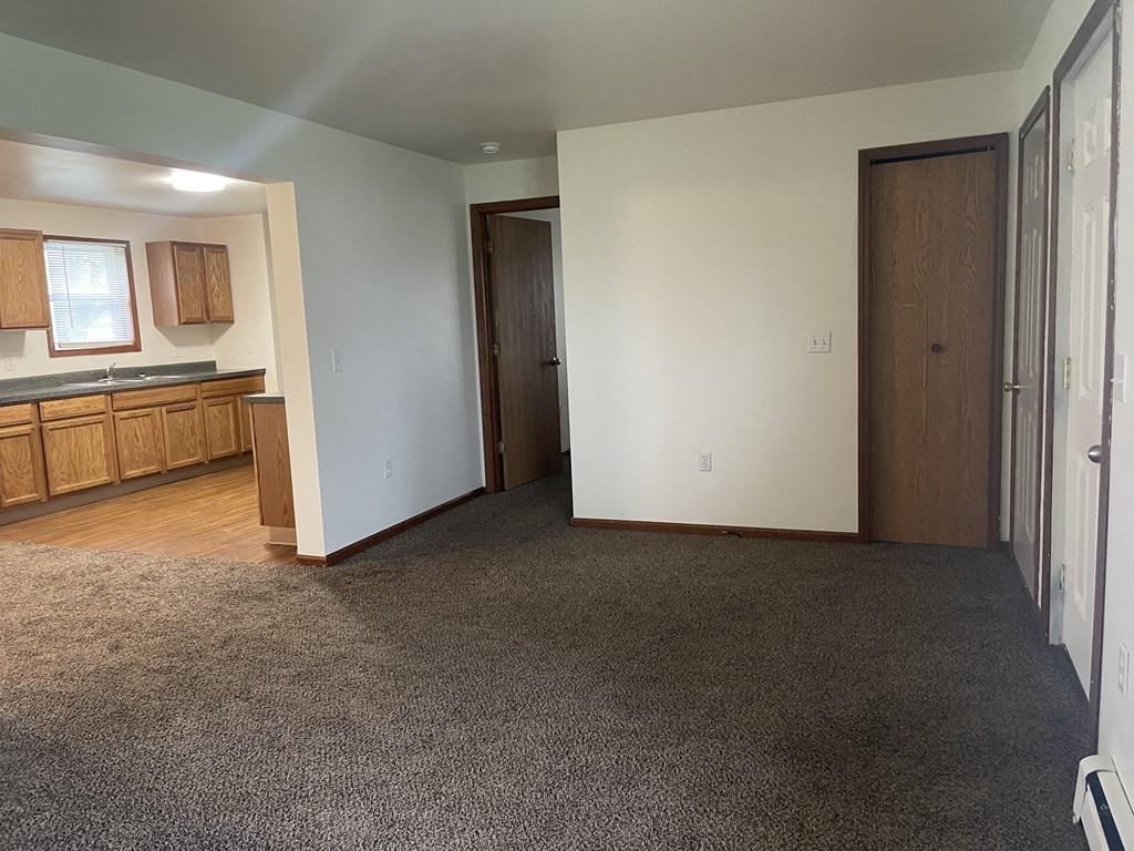 an empty living room with a kitchen in the background