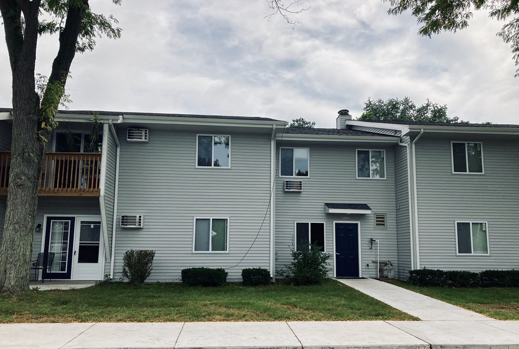 a white house with a sidewalk and a tree in front of it