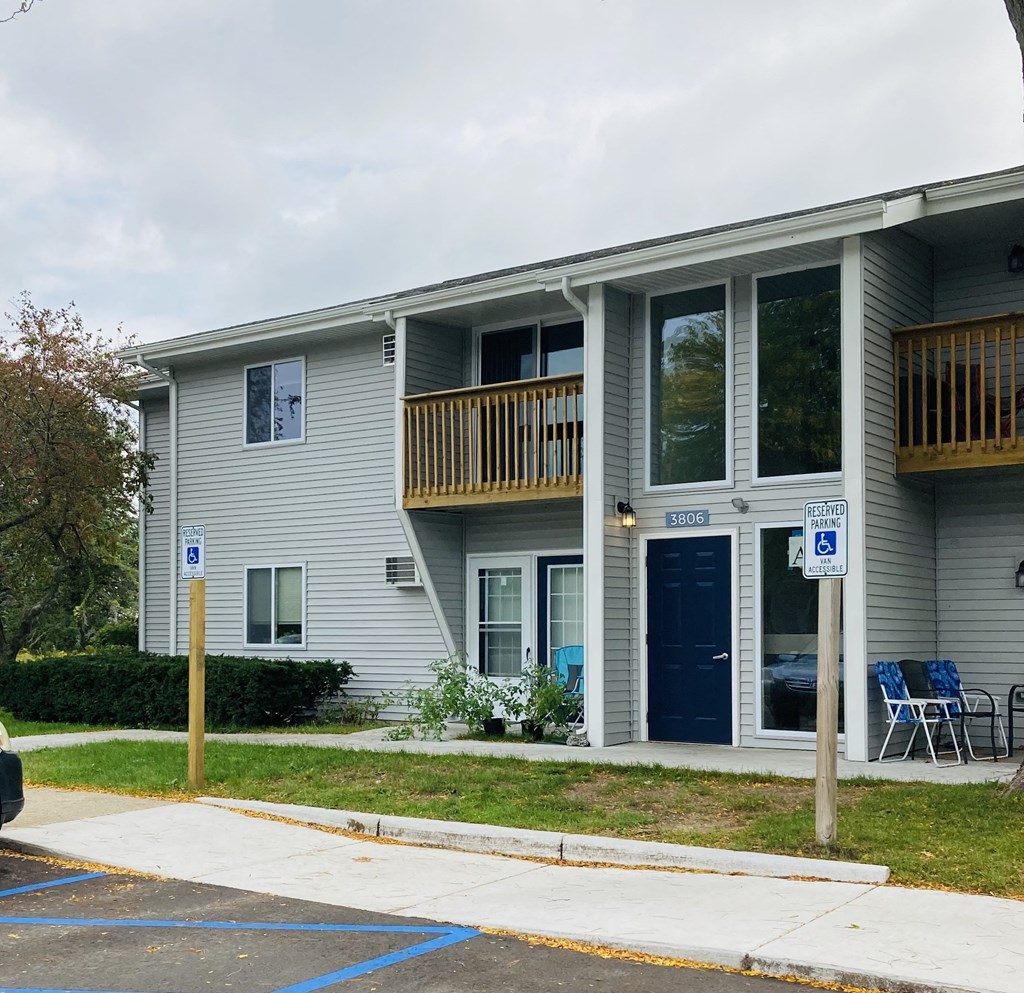 the exterior of an apartment building with a porch and blue chairs