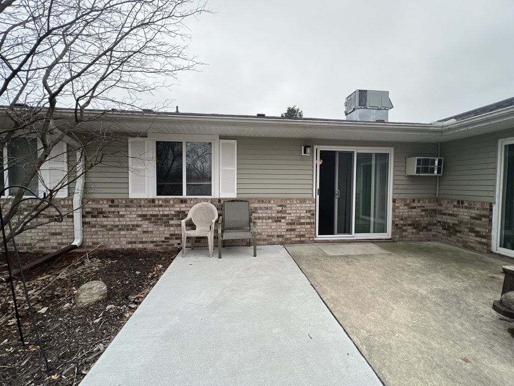 a home with a concrete walkway leading to a door with an air conditioner on the