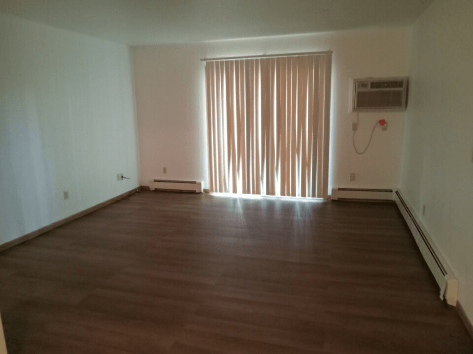 an empty room with wooden floors and a large window with vertical blinds