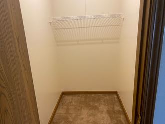a small walk in closet with a metal shelf and a carpeted floor