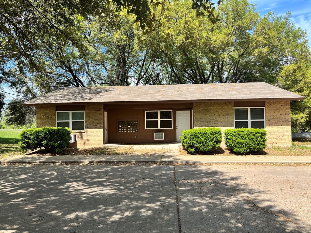 a small brick house with a driveway and trees in the background