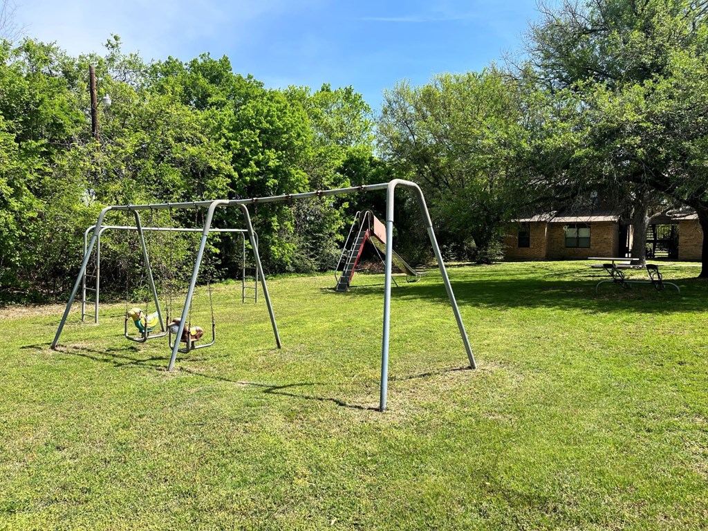 a swing set in a grassy area with trees in the background