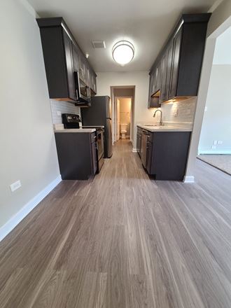 a kitchen and hallway in a new home with black cabinets and wood floors