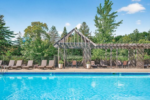 A pool with a wooden structure and chairs around it.