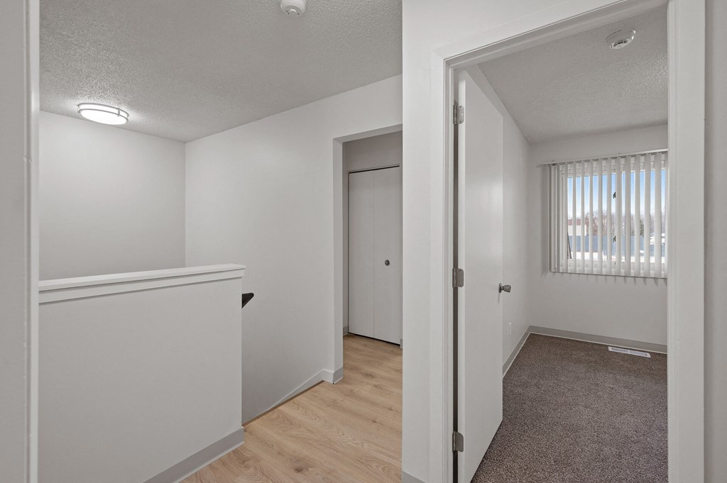 the living room and dining room of an apartment with white walls and wood flooring