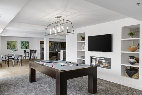 A pool table is in the middle of a room with a tv on the wall.