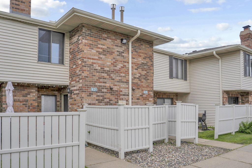 A white picket fence separates a house from a brick building.