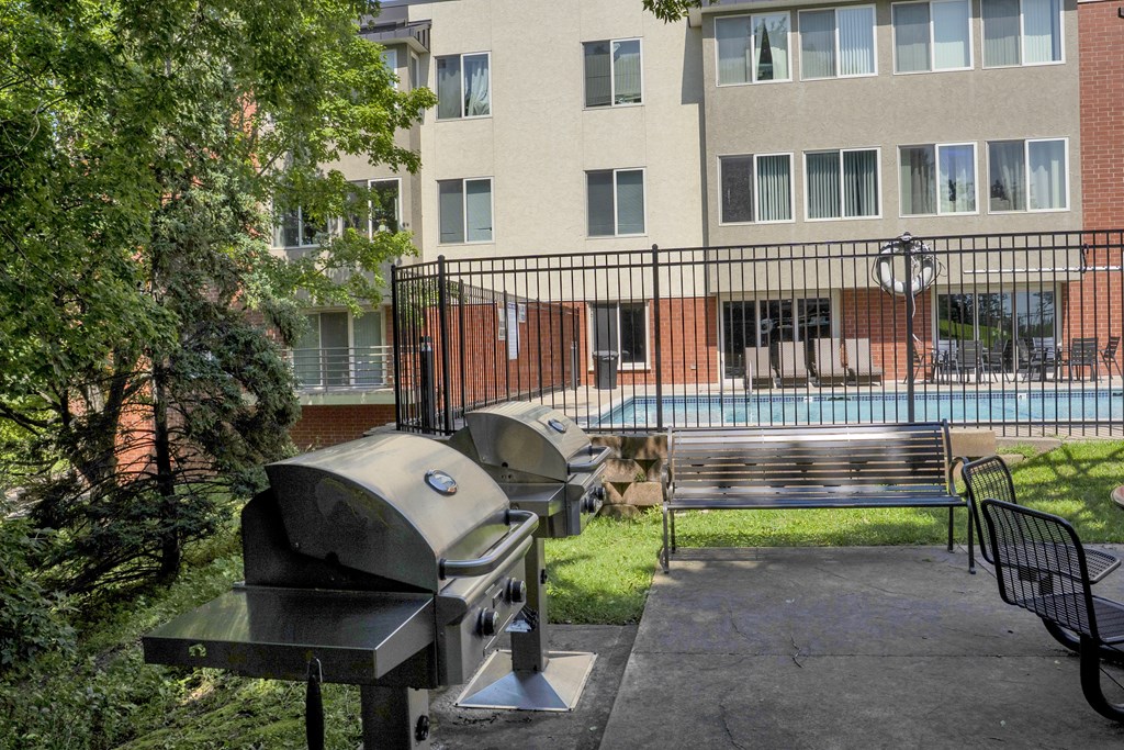 A BBQ grill is in the foreground of a courtyard with a pool and apartment building in the background.