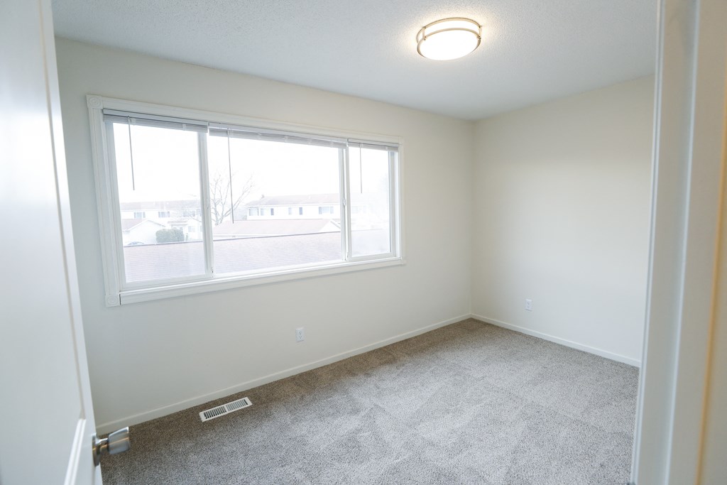 an empty bedroom with a large window and carpeting