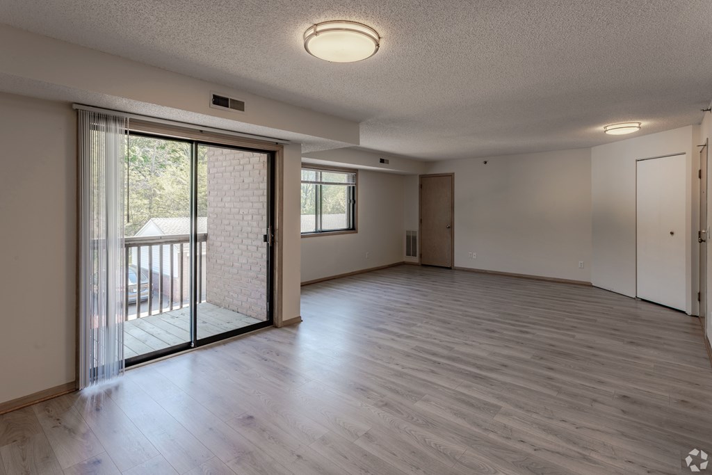 A spacious room with wooden flooring and sliding glass doors leading to a balcony.