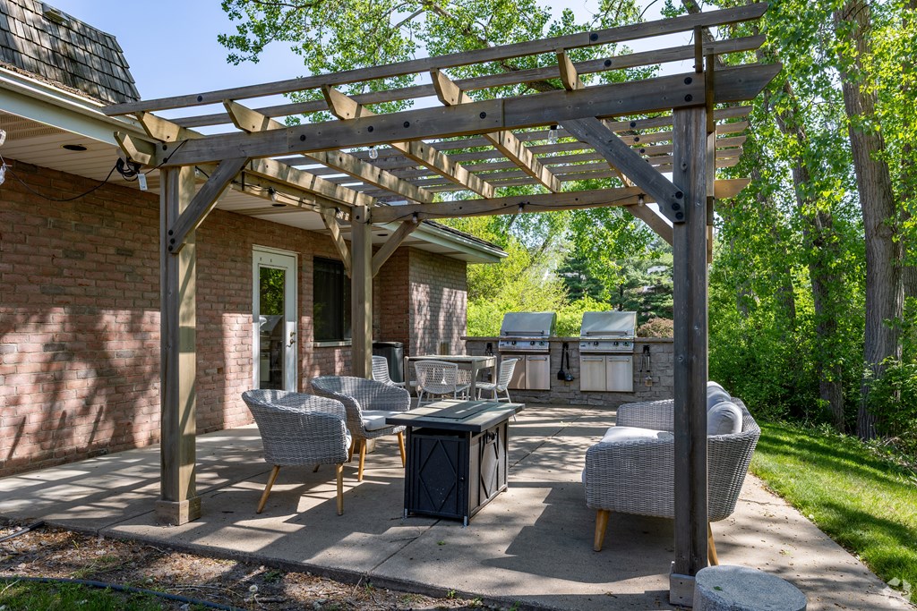 A wooden pergola is over a patio with chairs and a table.