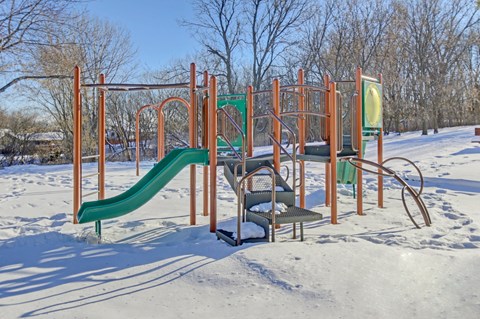 A playground with a green slide and orange structure in the snow.
