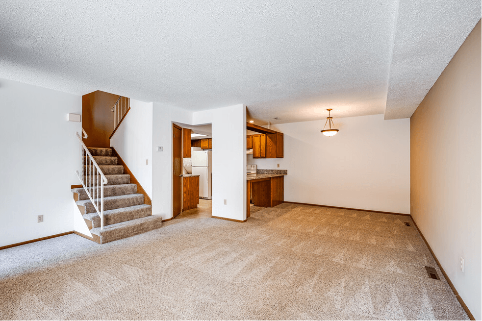 an empty living room with a staircase and a kitchen in the background