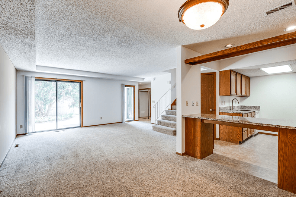 an empty living room with a kitchen and a staircase