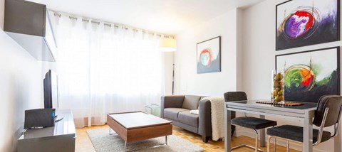 A living room with a grey couch, a black chair, a wooden coffee table, a television, and a painting on the wall.