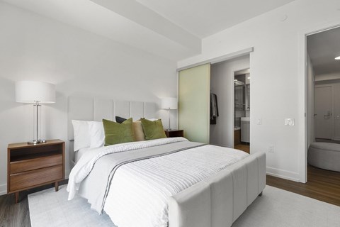 A white bed with a white mattress and a white bed sheet with a white pillow and a white lamp on a wooden nightstand.