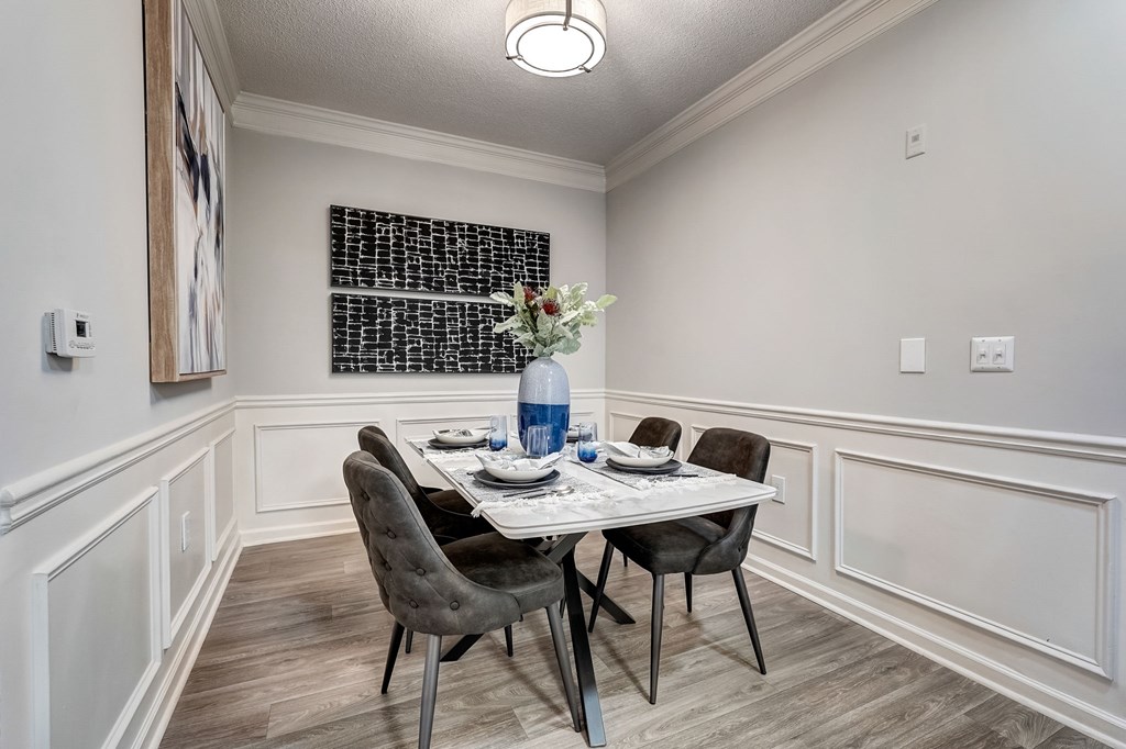 A dining room with a table set for two and a vase of flowers.
