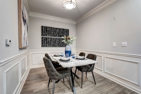 A dining room with a table set for two and a vase of flowers.