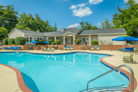 A large swimming pool in front of a house with a blue umbrella.