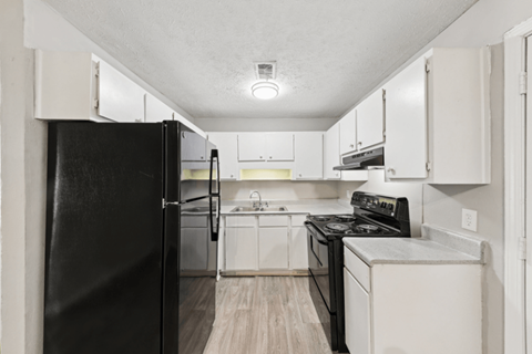 A black refrigerator is in a kitchen with white cabinets.