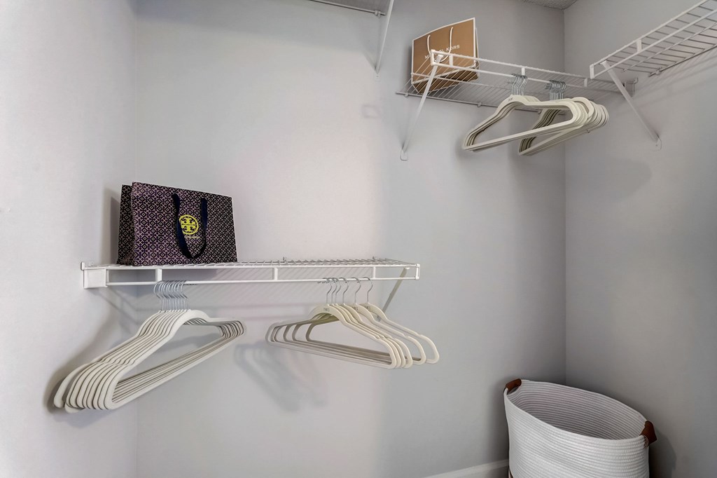 A white closet with hangers and a bag on the shelf.
