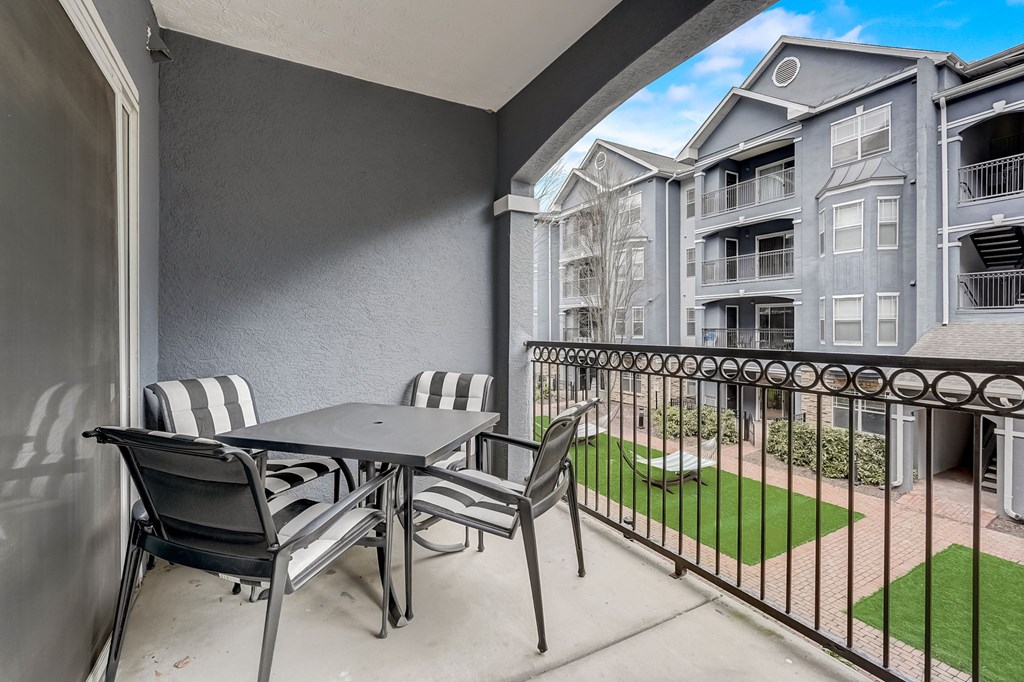 A patio with a table and chairs overlooks a grassy area and apartment buildings.