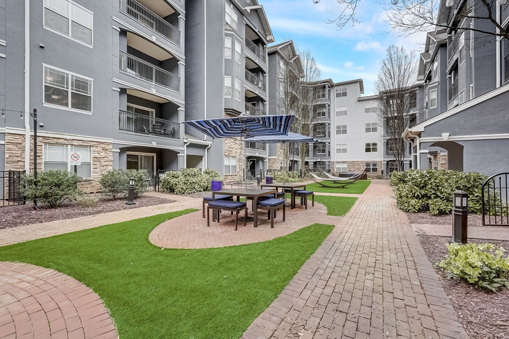 A patio with a table and chairs is surrounded by a brick walkway and a grassy area.