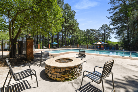 A pool surrounded by trees and chairs.