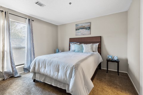 A bedroom with a large bed and a small table with a clock on it.