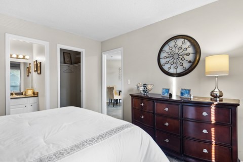 A bedroom with a white bed and a brown dresser.