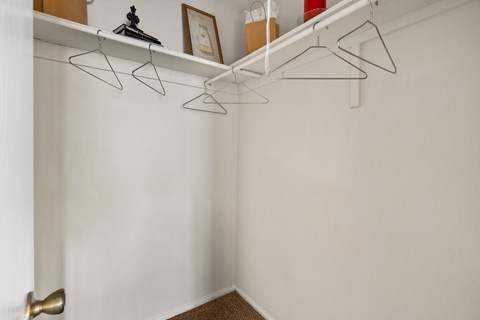 A white wall with a gold door knob and a shelf with three hangers.