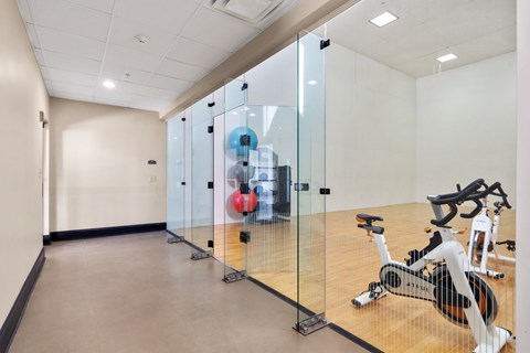 A room with a row of stationary bikes and a glass wall.