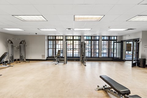 A gym with a bench, weights, and windows.