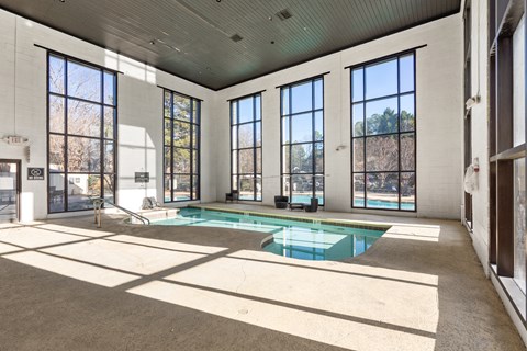 A large indoor swimming pool with a sunny day outside.