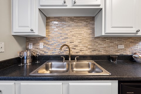 A kitchen with a double sink and a brick backsplash.