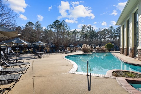 A pool surrounded by trees and a patio with chairs.