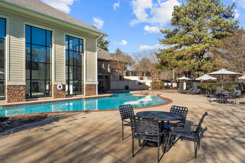 A patio with a table and chairs is in front of a house with a pool.