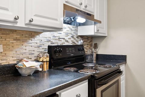 A black stove top oven with a glass cooktop sits in a kitchen with white cabinets.