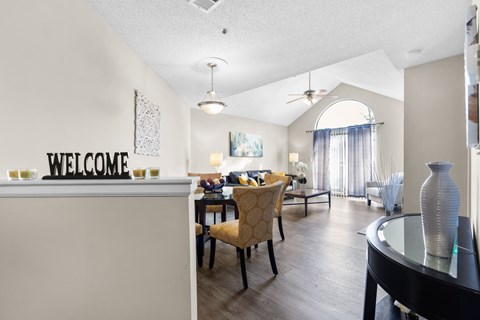 A dining room with a white wall that says "welcome" and a table with chairs.