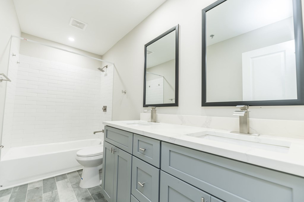 A white toilet sits in a bathroom with a white tub and a sink with a mirror above it.