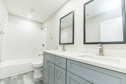 A white toilet sits in a bathroom with a white tub and a sink with a mirror above it.