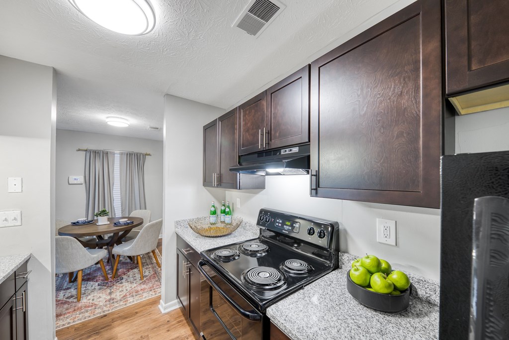 A kitchen with a stove top oven and a bowl of green apples on the counter.