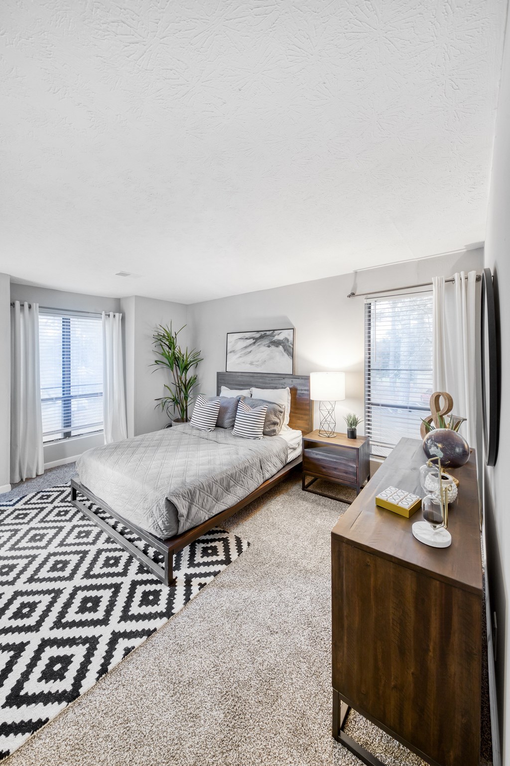 A bedroom with a bed, nightstand, and a rug with a geometric pattern.