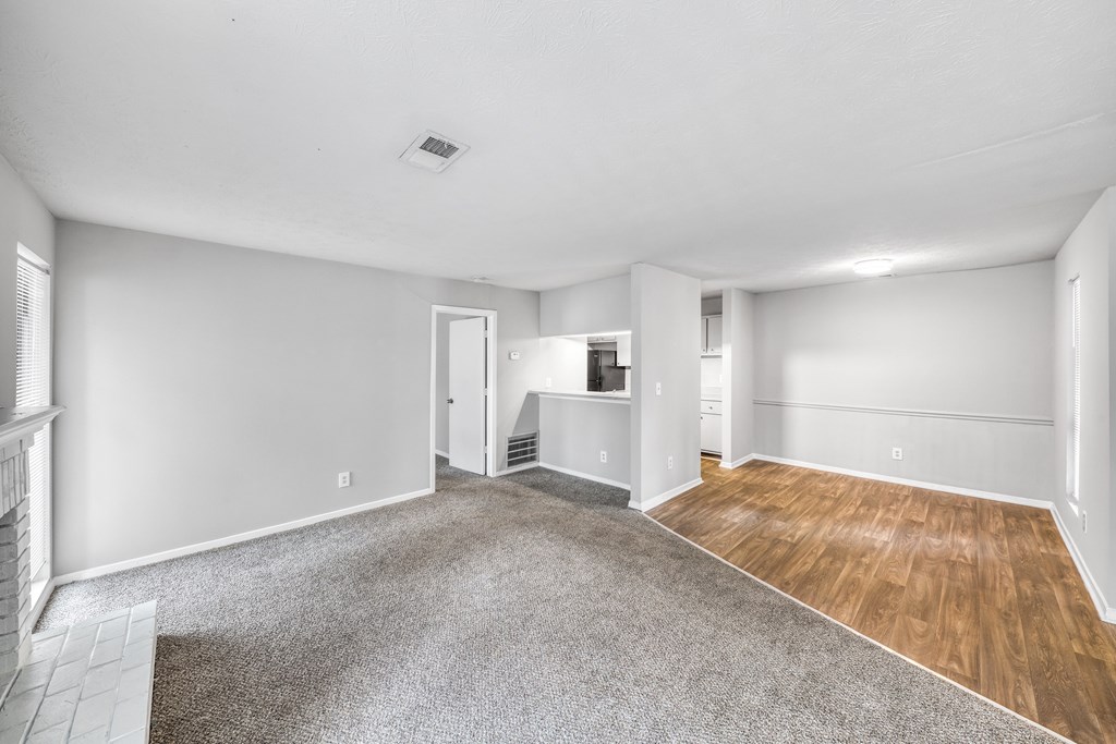A large empty room with a grey carpet and wooden flooring.